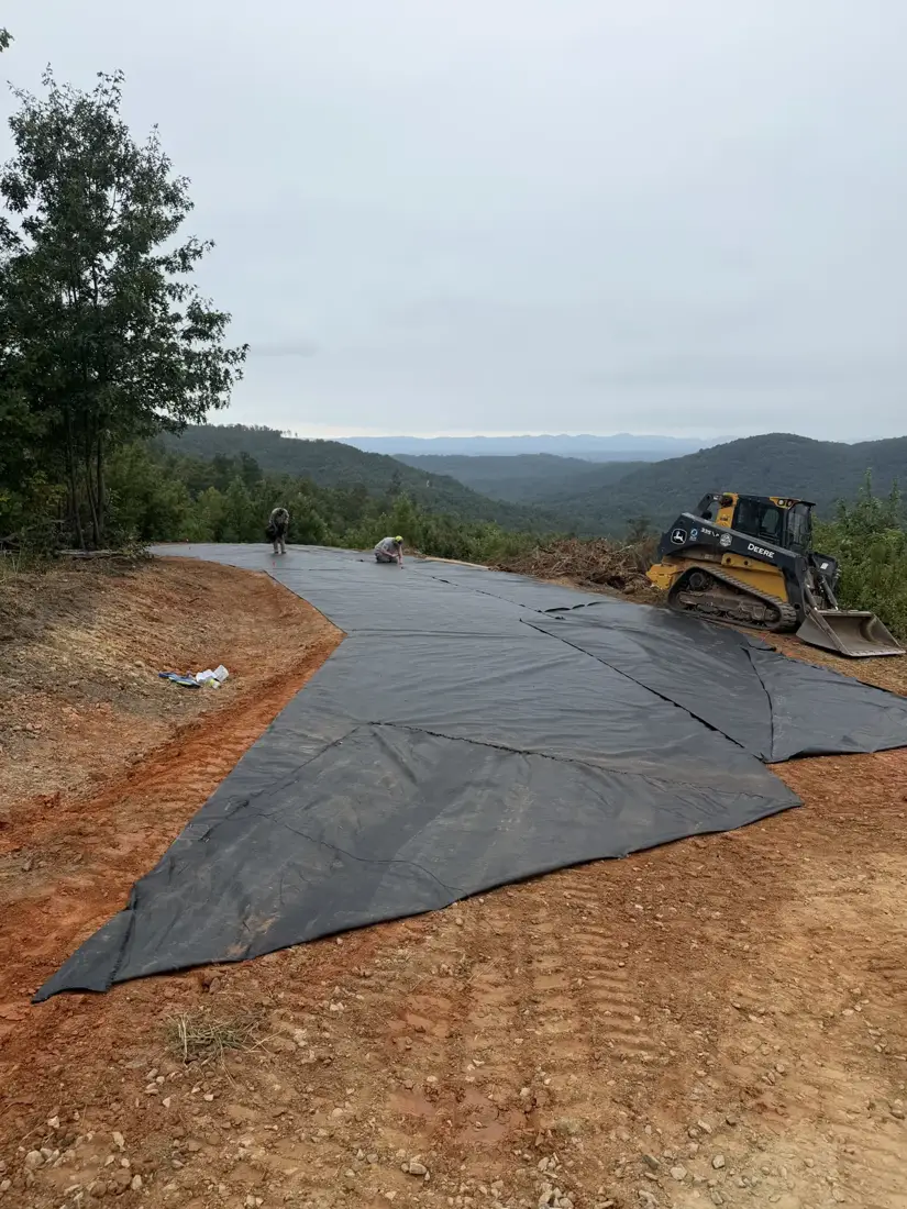 Crew placing geotextile fabric over a graded driveway base