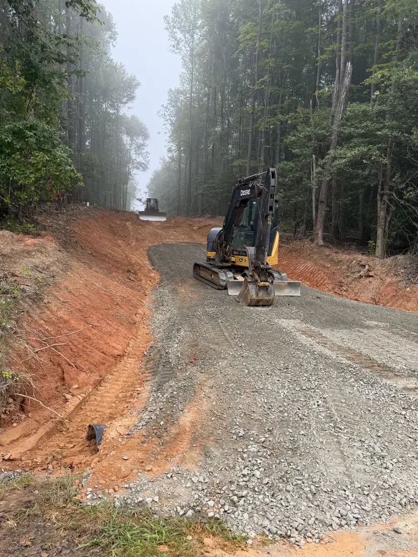 Excavator spreading gravel on a new driveway through the woods